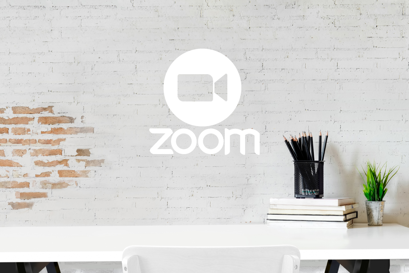 White brick wall, desk, chair with various stationary items with the zoom logo on top - White Canvas Design