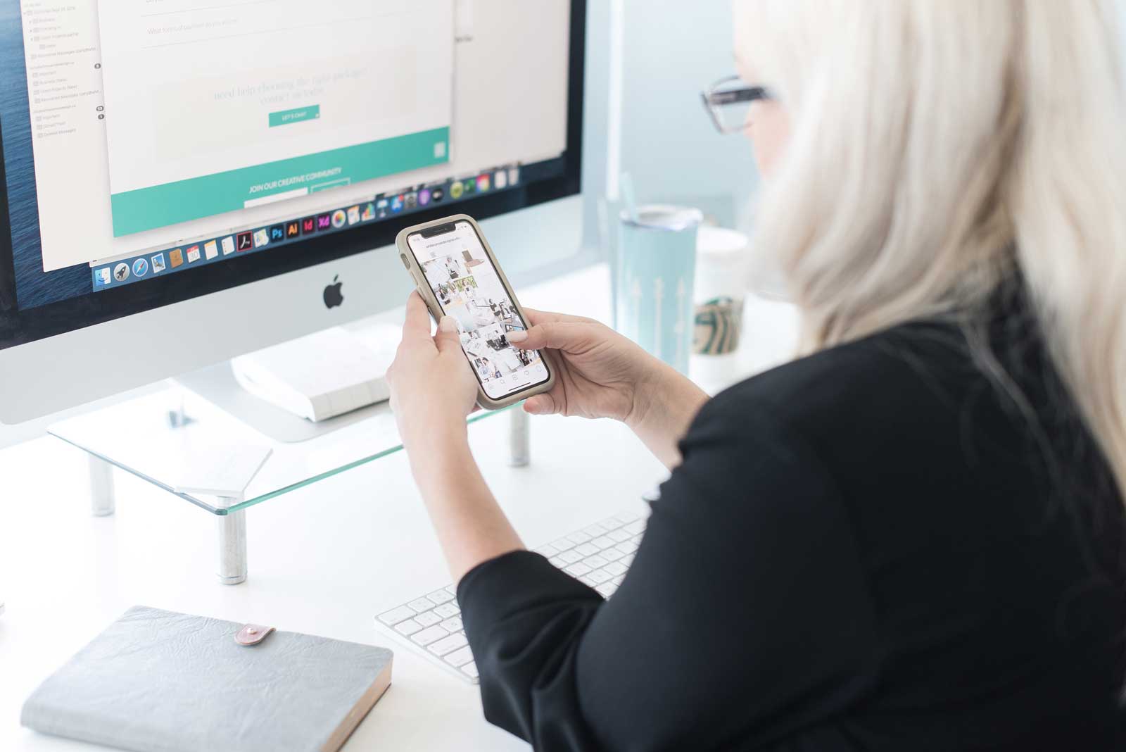 Woman at computer while looking at her phone