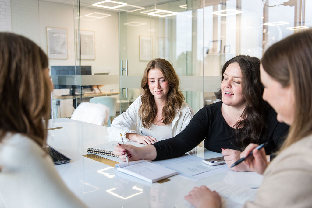 a group of women designers sitting around a table in an office, talking and smiling