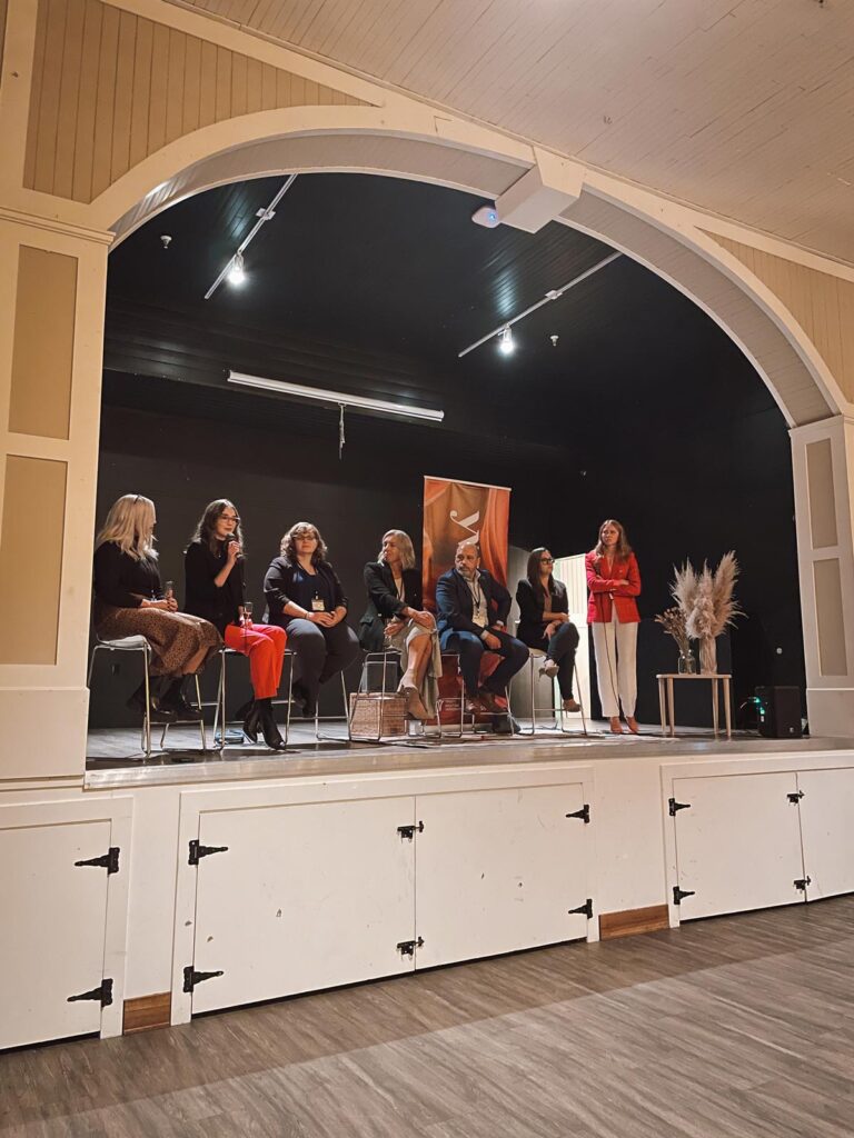 A panel of speakers sitting on a stage giving a talk